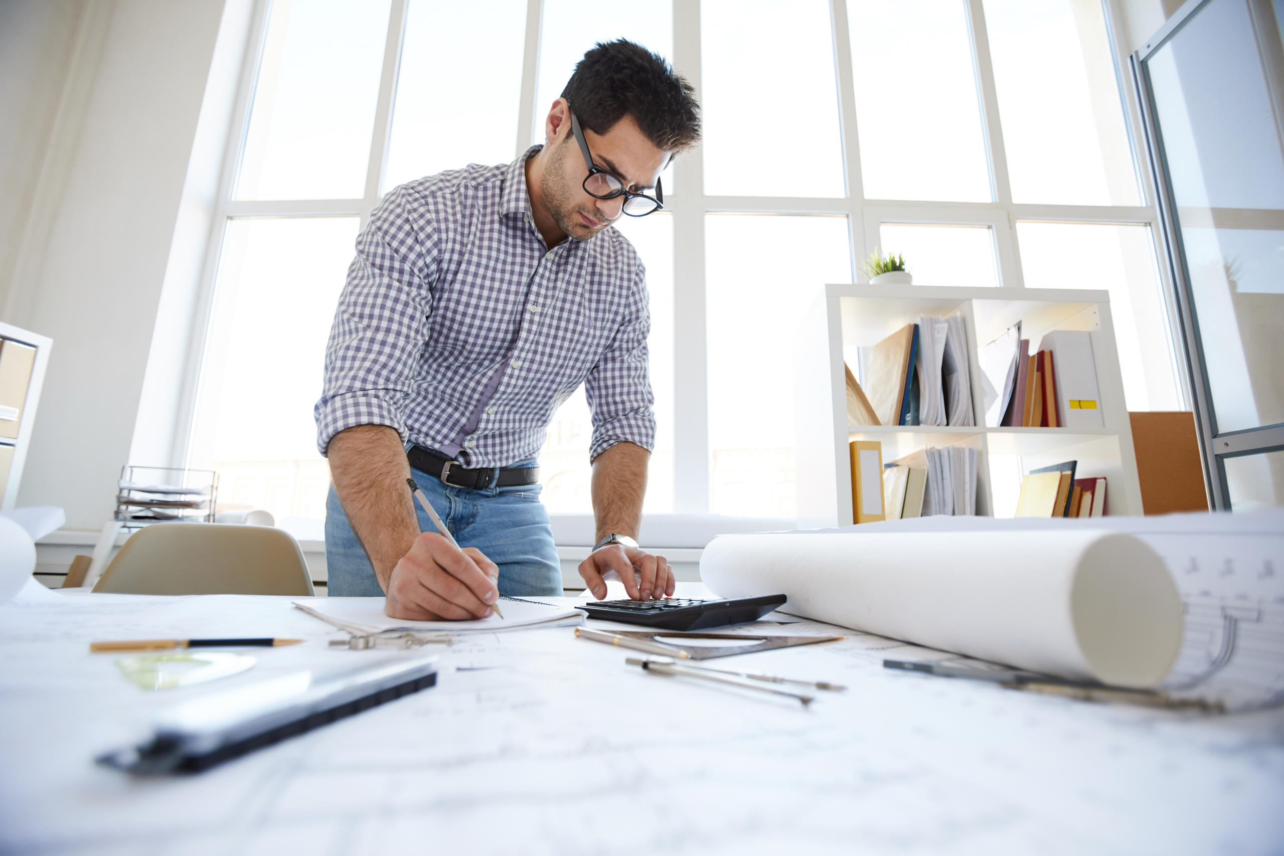 man working on engineering drawing plans with calculator and pencil
