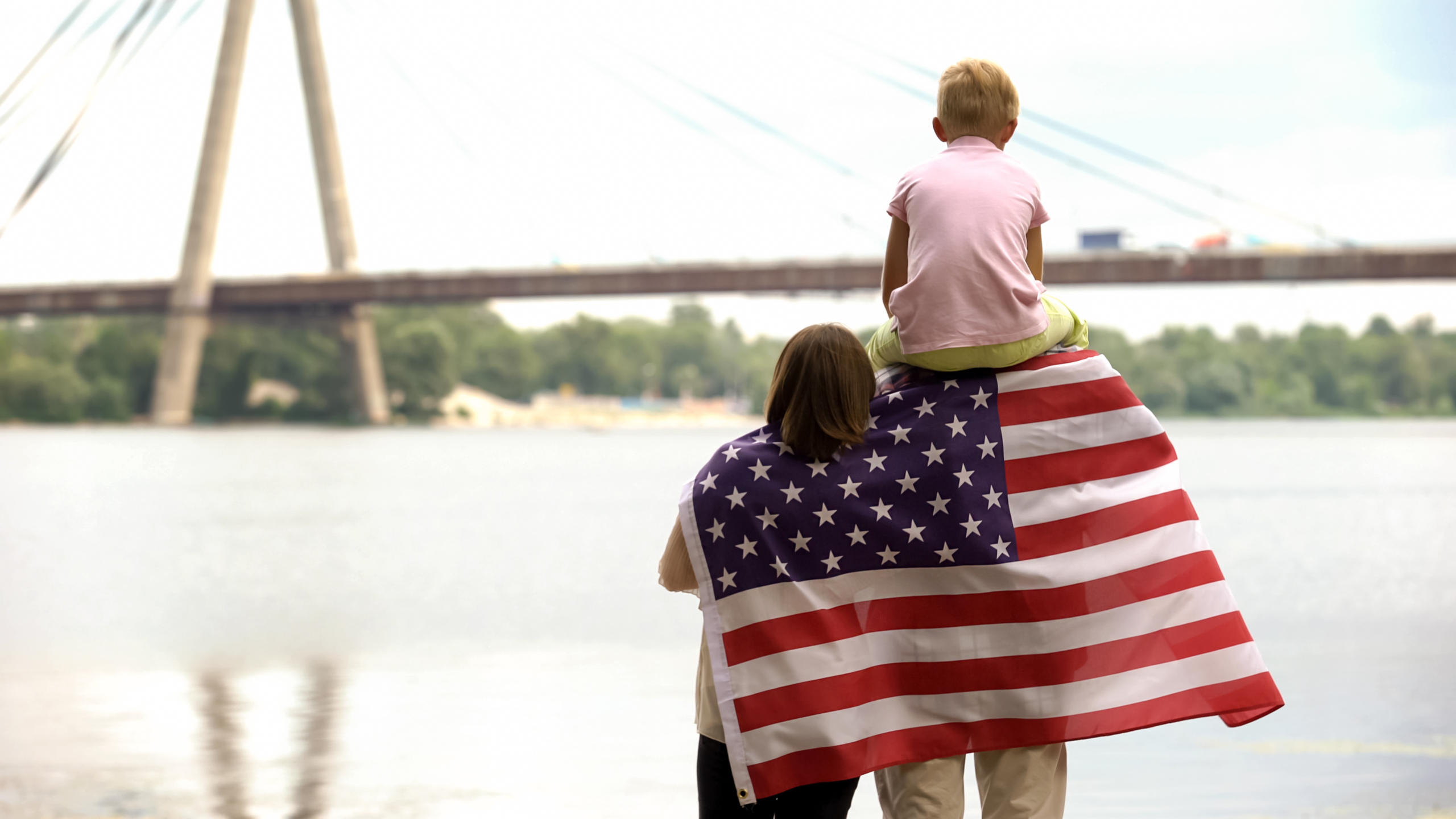 family looking at a river with american flag over the dad's shoulders