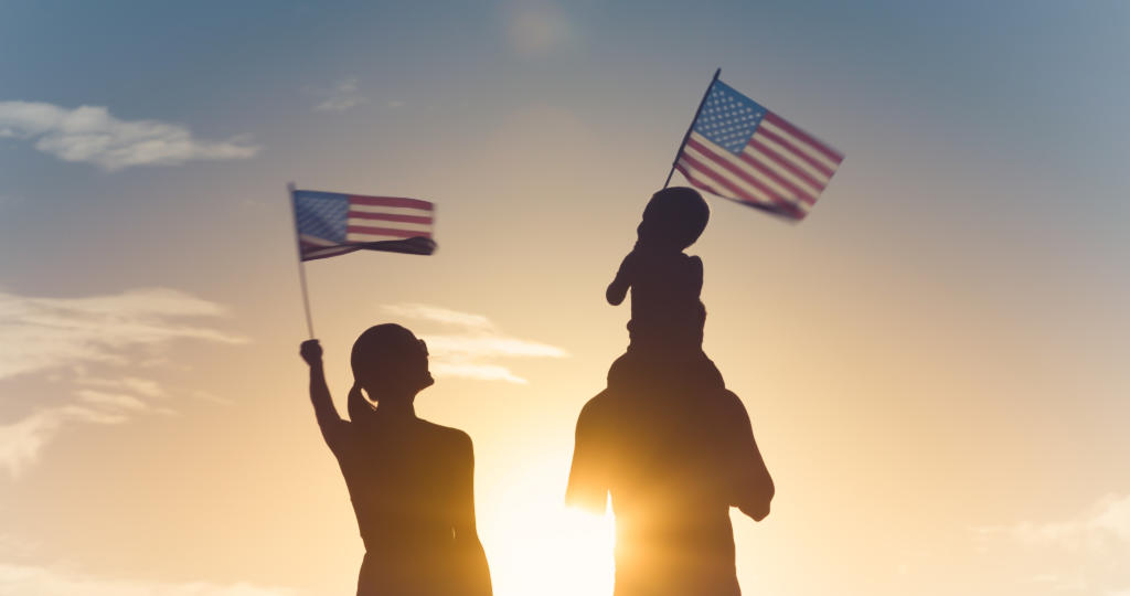 Patriotic man woman and child waving American flags in the air at sunset