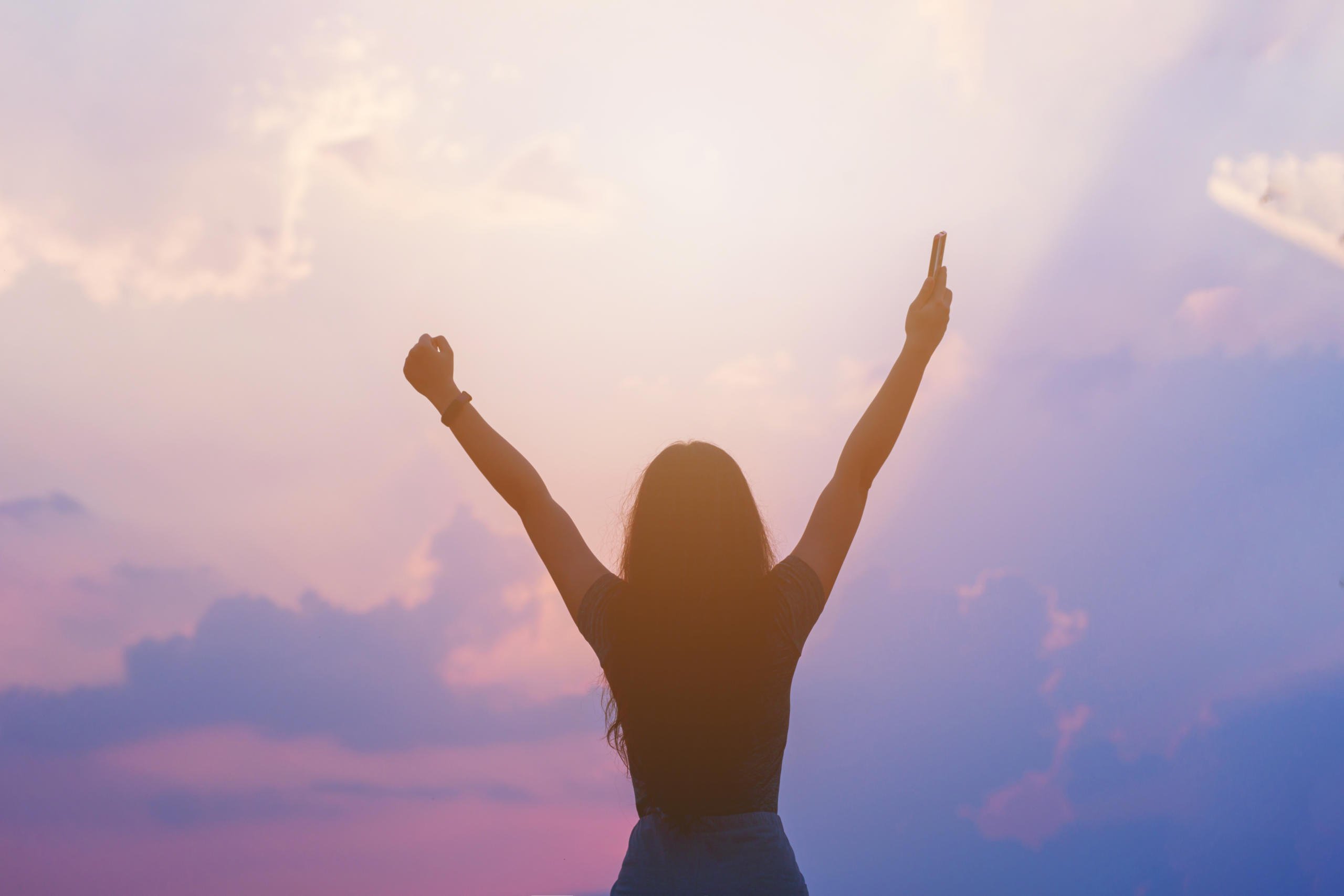 woman holding hand up in the air in excitement during sunset